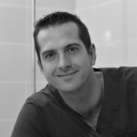 Formation continue en Dermatologie Vétérinaire depuis 25 ans ! Homme souriant en uniforme médical dans un environnement clinique en noir et blanc.